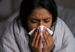 A woman holding a tissue while feeling sick, representing symptoms of illness or infection.