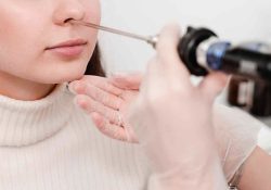 Close-up photo of a patient undergoing rigid nasal endoscopy. A doctor wearing gloves gently inserts a straight endoscope into the patient’s nostril for examining nasal passages, capturing live images on a nearby monitor.